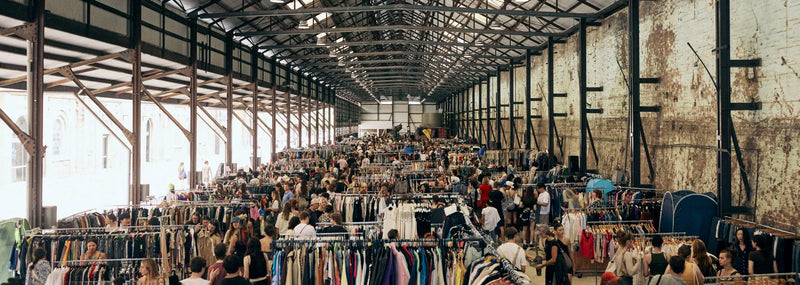 Large indoor market with people browsing through vintage clothing racks.