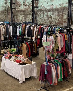 Vintage clothing stall with racks of clothes and handbags against a textured wall.