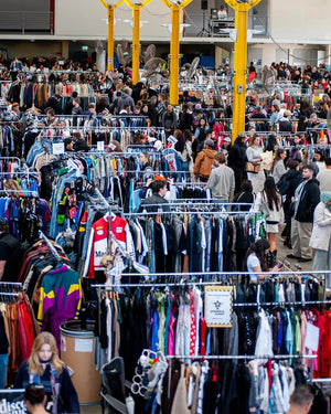 Crowded indoor vintage market with clothing racks and people shopping.