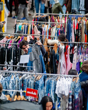 People shopping at a vintage flea market with racks of clothing.