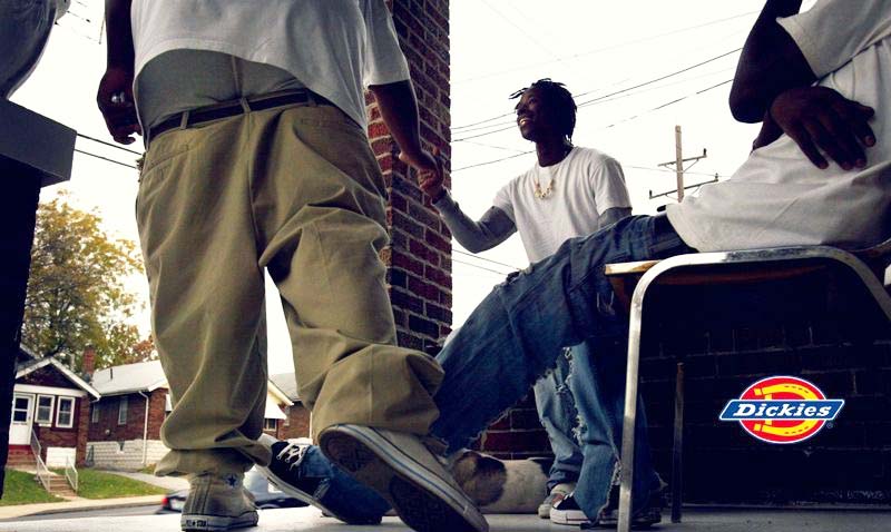 Two men sitting on a chair with a Dickies logo in an urban setting