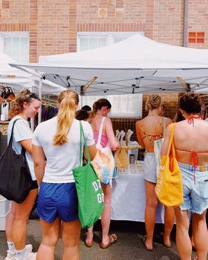 People shopping at an outdoor market under a white tent.