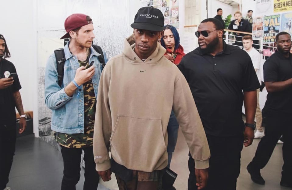 Man in a beige vintage  Nike hoodie walking through a crowd in an indoor setting