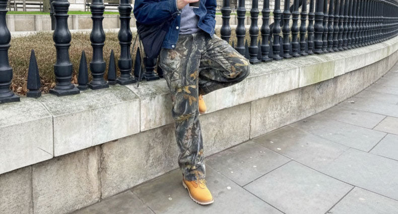 Person sitting on a stone wall wearing vintage  Realtree camouflage pants and yellow boots.