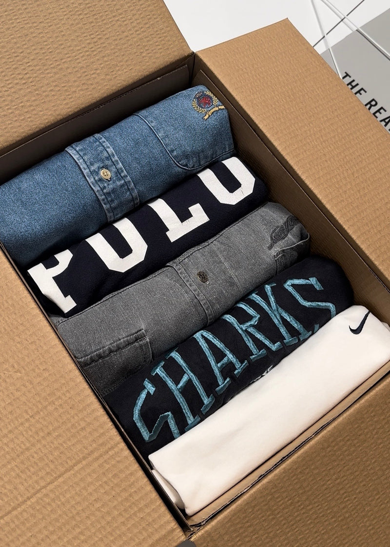 Vintage Mystery Box containing folded Polo T-Shirt, Levi's Denim Button Up Shirt, Nike Swoosh Sweatshirt, San Jose Sharks T-Shirt, and Tommy Hilfiger Denim Button Up Shirt on a white bench in a warehouse