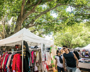 Outdoor vintage market with stalls under trees, people browsing clothes.